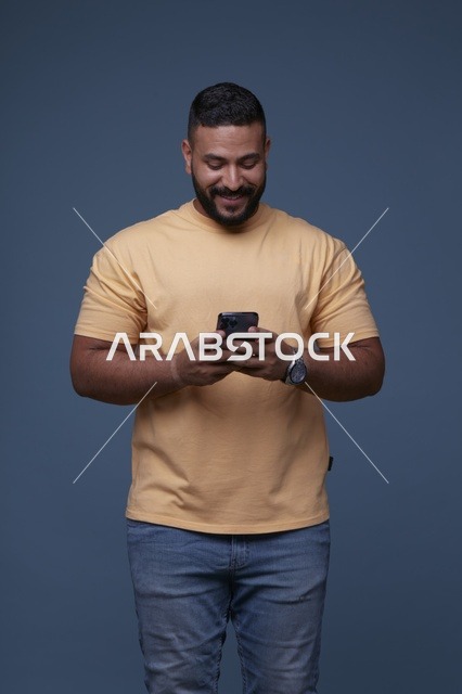 رجل سعودي بملابس كاجوال يكتب على الهاتف الذكي في استوديو