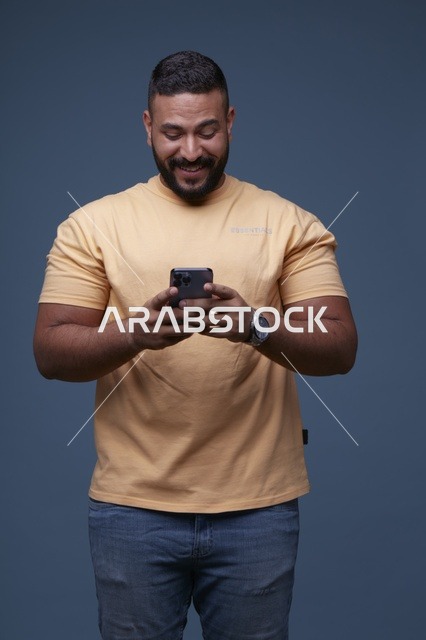 رجل سعودي يستخدم الهاتف الذكي بملابس كاجوال في الاستوديو