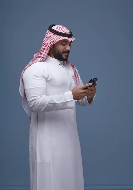 رجل سعودي مبتسم بالزي التقليدي يستخدم الهاتف الذكي