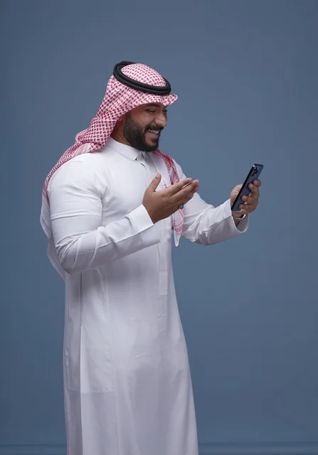 Smiling Saudi Man in Traditional Thobe Using Smartphone