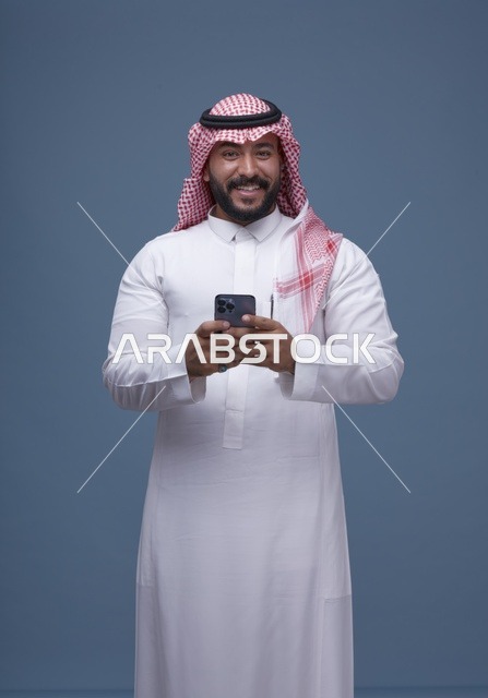 رجل سعودي مبتسم يستخدم الهاتف الذكي بالزي التقليدي