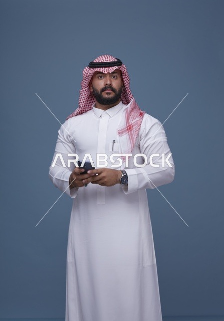 رجل سعودي بالزي التقليدي يمسك هاتف ذكي في الاستوديو