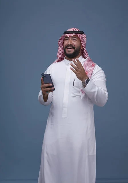 رجل سعودي بالزي التقليدي يستخدم الهاتف الذكي في استوديو