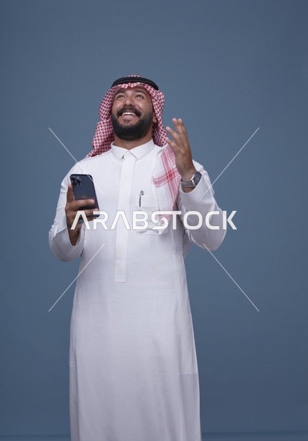 رجل سعودي مبتسم يرتدي الزي التقليدي مع هاتف ذكي