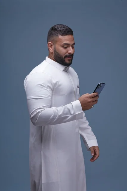 Saudi Man in White Thobe Using Smartphone
