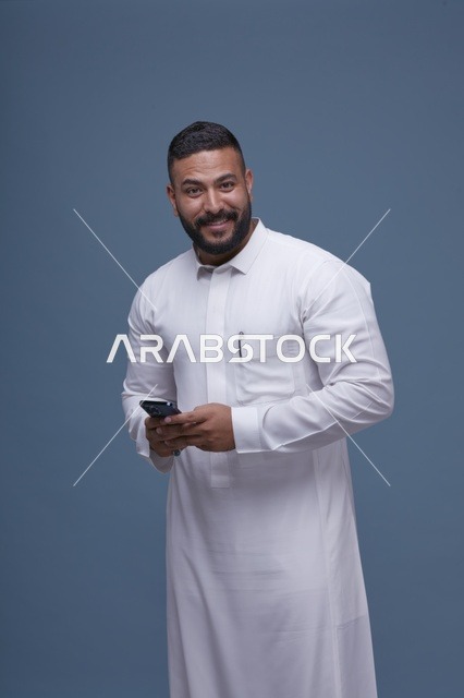 رجل سعودي بالثوب الأبيض يمسك هاتفاً ذكياً بخلفية زرقاء