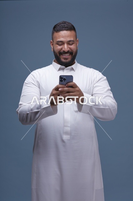 رجل سعودي بالثوب الأبيض يستخدم الهاتف الذكي في الاستوديو