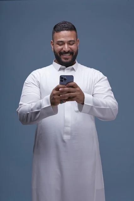 رجل سعودي بالثوب الأبيض يستخدم الهاتف الذكي في الاستوديو