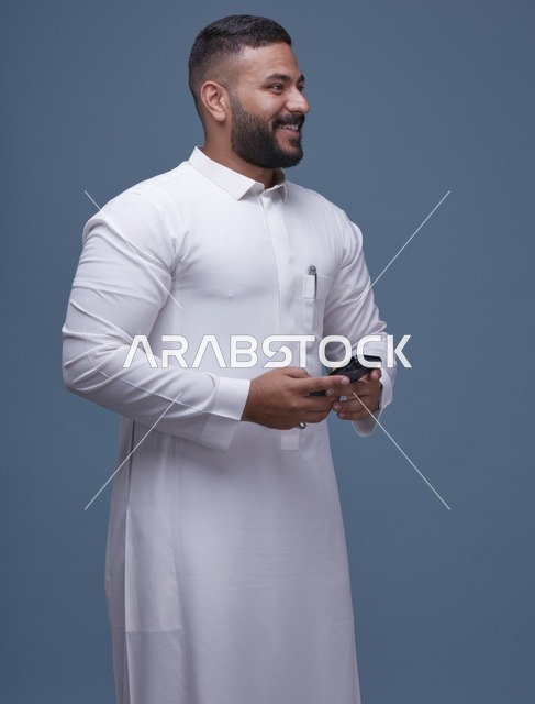 رجل سعودي بالثوب الأبيض يستخدم الهاتف الذكي خلفية زرقاء