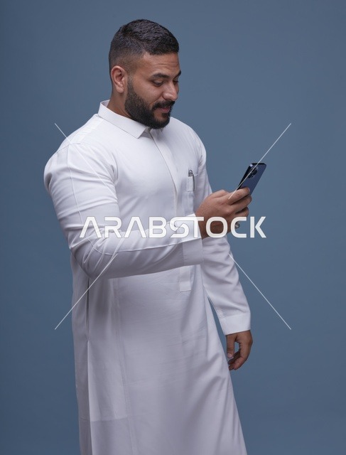 رجل سعودي بالثوب الأبيض يستخدم الهاتف الذكي في الاستوديو