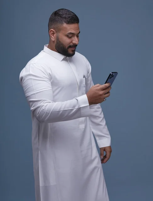 رجل سعودي بالثوب الأبيض يستخدم الهاتف الذكي في الاستوديو