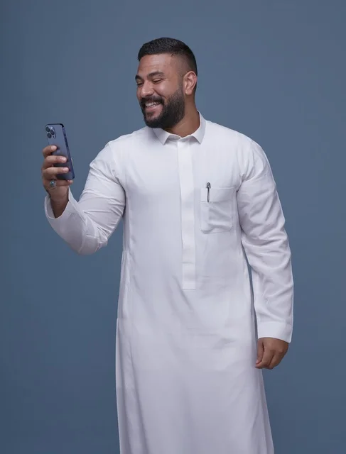 رجل سعودي يرتدي الثوب الأبيض يستخدم الهاتف الذكي بخلفية زرقاء