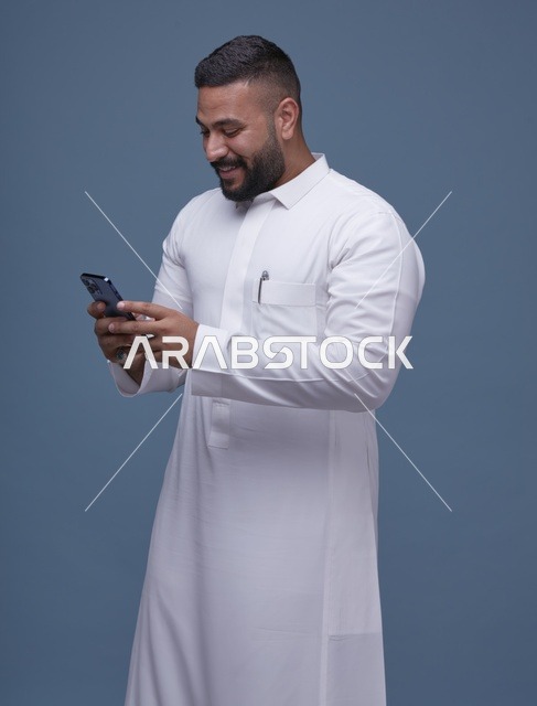 رجل سعودي بالثوب الأبيض يستخدم الهاتف الذكي في استوديو