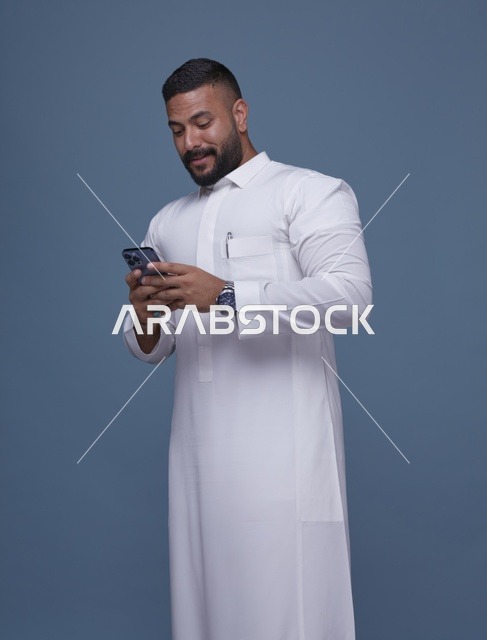 رجل سعودي بالثوب الأبيض يستخدم الهاتف الذكي في الاستوديو