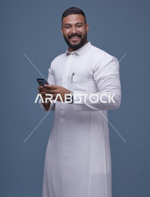 رجل سعودي يرتدي الثوب الأبيض ويستخدم الهاتف الذكي في استوديو