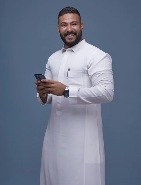 رجل سعودي يرتدي الثوب الأبيض ويستخدم الهاتف الذكي في استوديو