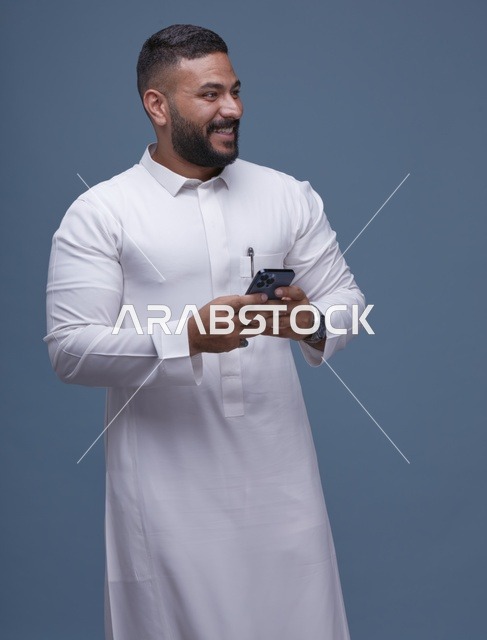 رجل سعودي بالثوب الأبيض يستخدم الهاتف الذكي في استوديو
