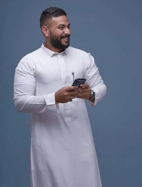 رجل سعودي بالثوب الأبيض يستخدم الهاتف الذكي في استوديو