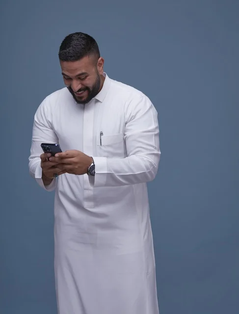 Saudi Man in White Thobe Using Smartphone