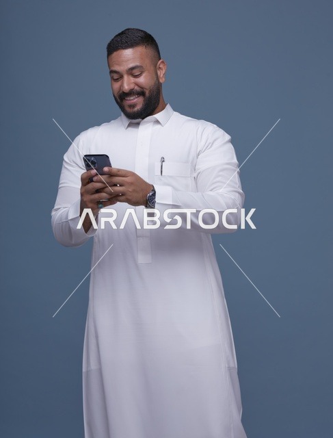 رجل سعودي بالثوب الأبيض يستخدم الهاتف الذكي في الاستوديو