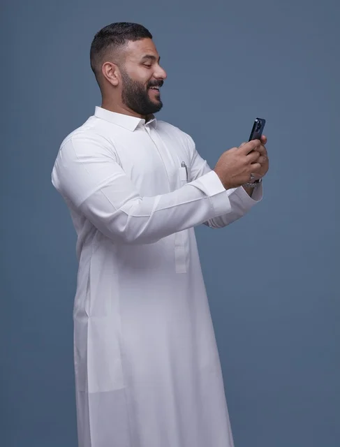 Saudi Man in White Thobe Using Smartphone