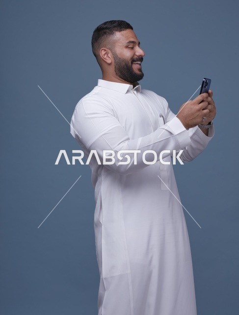 رجل سعودي يستخدم الهاتف الذكي مرتدياً ثوباً أبيض