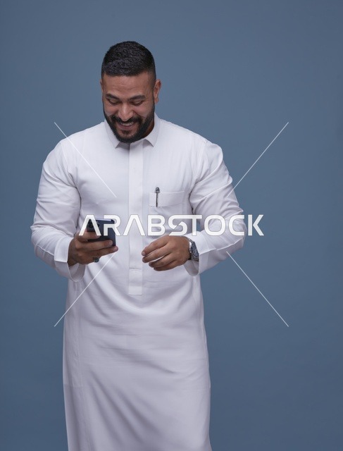 رجل سعودي بالثوب الأبيض يستخدم الهاتف الذكي في الاستوديو