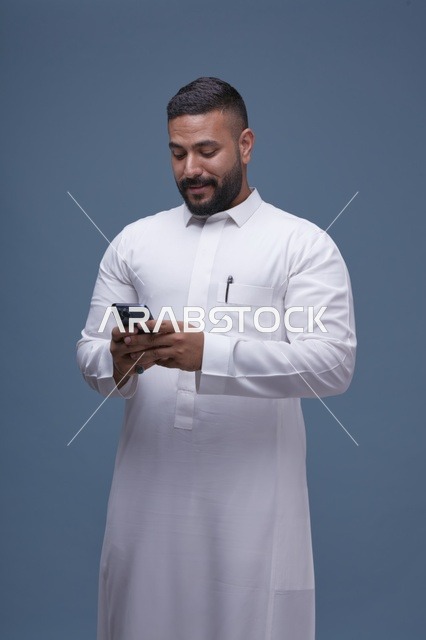 رجل سعودي بالثوب الأبيض يستخدم الهاتف الذكي في استوديو