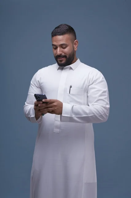 رجل سعودي بالثوب الأبيض يستخدم الهاتف الذكي في استوديو