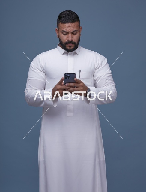 رجل سعودي بالثوب الأبيض يستخدم الهاتف الذكي في الاستوديو