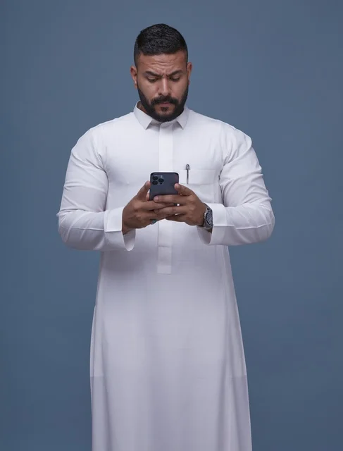 رجل سعودي بالثوب الأبيض يستخدم الهاتف الذكي في الاستوديو