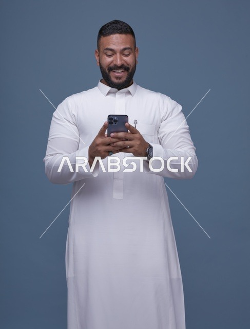 رجل سعودي يستخدم الهاتف الذكي مرتدياً الثوب الأبيض