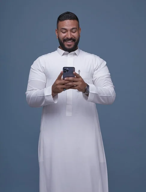 رجل سعودي يستخدم الهاتف الذكي مرتدياً الثوب الأبيض