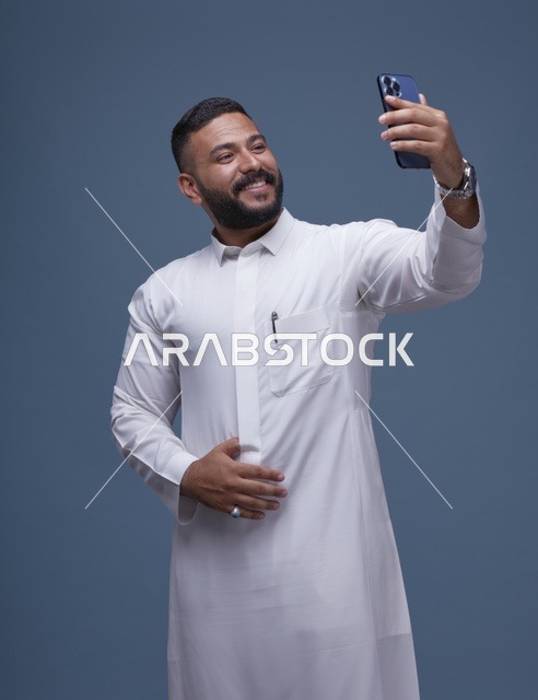رجل سعودي مبتسم يلتقط سيلفي بالثوب الأبيض