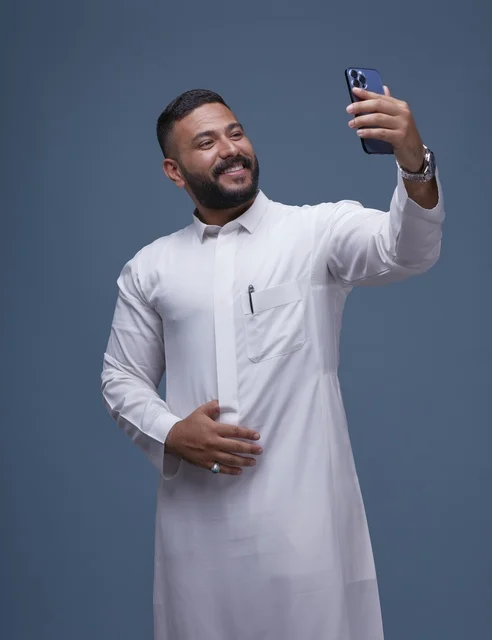 رجل سعودي مبتسم يلتقط سيلفي بالثوب الأبيض