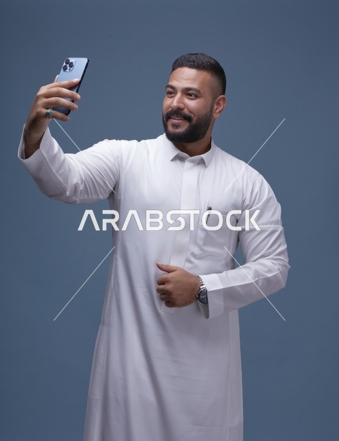 رجل سعودي يرتدي الثوب الأبيض يلتقط سيلفي بالهاتف