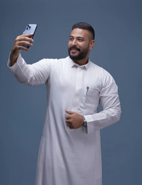 رجل سعودي يرتدي الثوب الأبيض يلتقط سيلفي بالهاتف