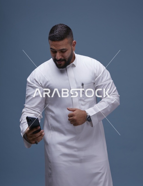 رجل سعودي مبتسم بالثوب الأبيض يلتقط سيلفي بالهاتف