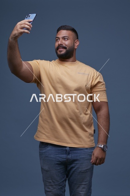 رجل سعودي يلتقط سيلفي بقميص أصفر خلفية زرقاء