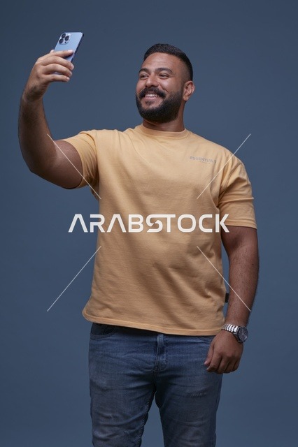 رجل سعودي بملابس كاجوال يلتقط صورة سيلفي بهاتف ذكي