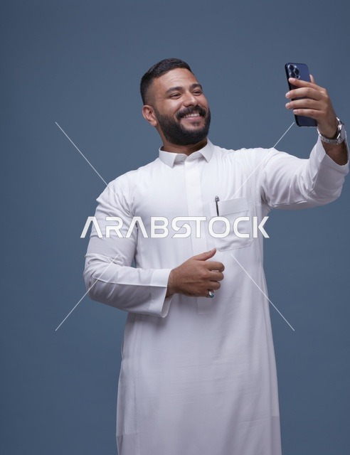 رجل سعودي مبتسم بالثوب الأبيض يلتقط صورة سيلفي