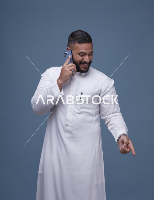 رجل سعودي بالثوب الأبيض يتحدث عبر الهاتف الذكي
