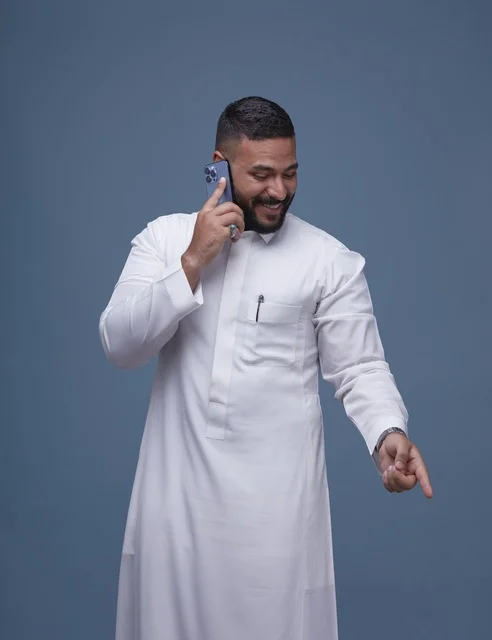 رجل سعودي بالثوب الأبيض يتحدث عبر الهاتف الذكي