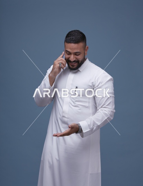 رجل سعودي يرتدي الثوب الأبيض يتحدث عبر الهاتف الذكي