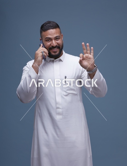 رجل سعودي بالثوب الأبيض يتحدث بالهاتف الذكي في استوديو