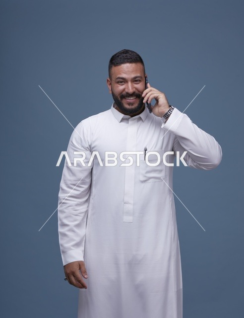رجل سعودي بالثوب الأبيض يتحدث بالجوال خلفية زرقاء