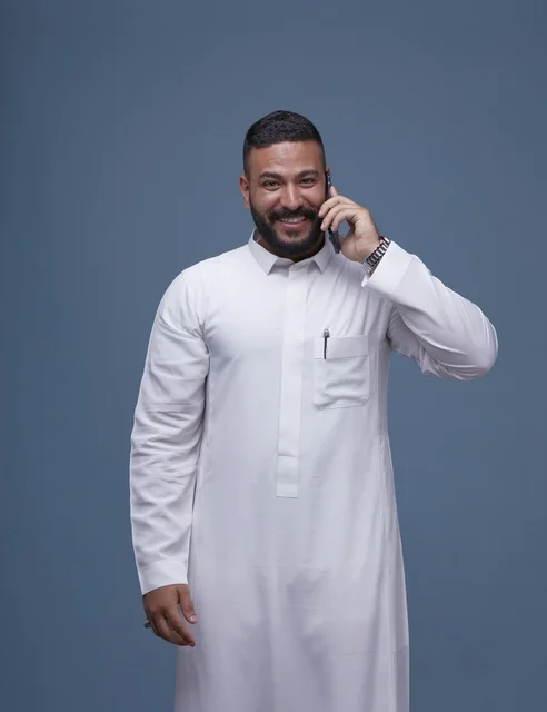 رجل سعودي بالثوب الأبيض يتحدث بالجوال خلفية زرقاء