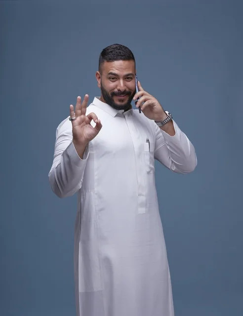 Saudi Man in White Thobe Using Smartphone with OK Gesture