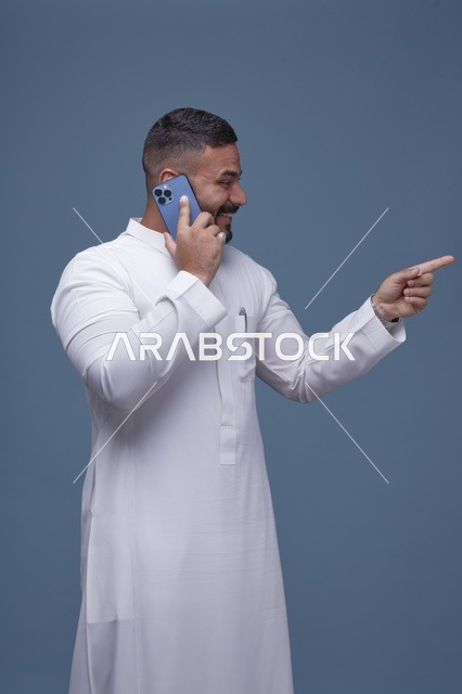 رجل سعودي بالثوب يتحدث عبر الجوال ويشير بيده