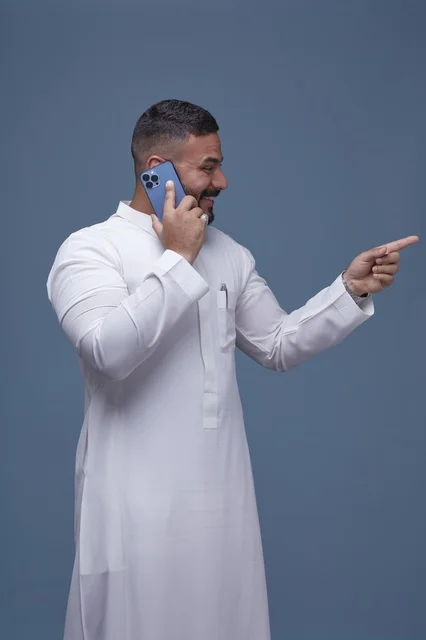 Saudi Man in White Thobe Talking on Smartphone